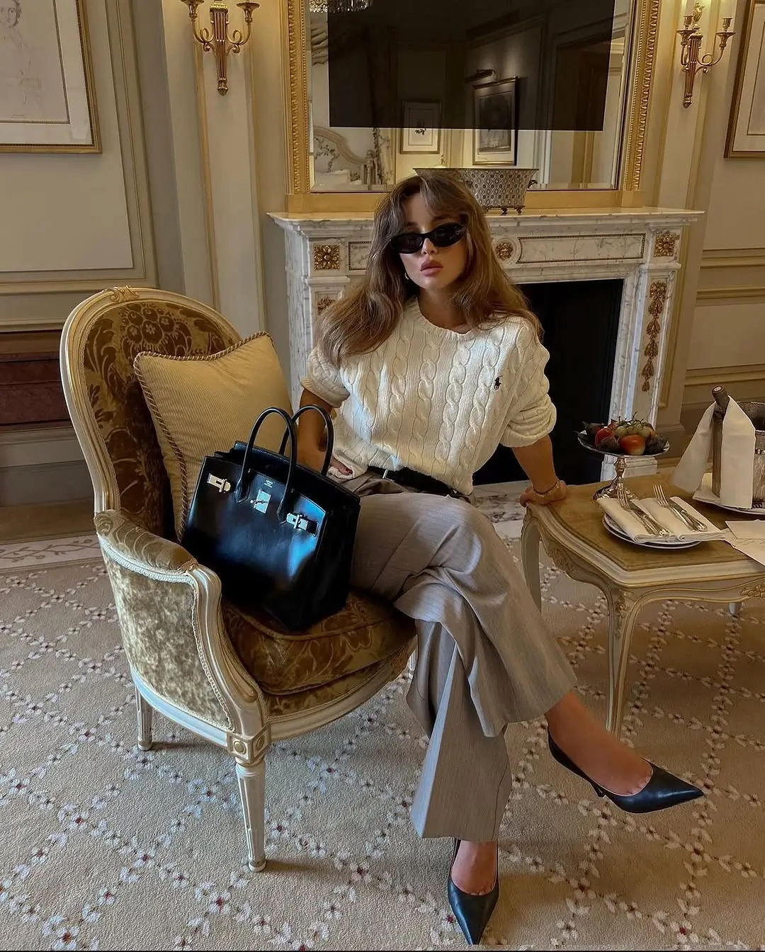 кремовий в'язаний джемпер із широкими сірими штанами і сумкою Birkin в готельному інтер'єрі