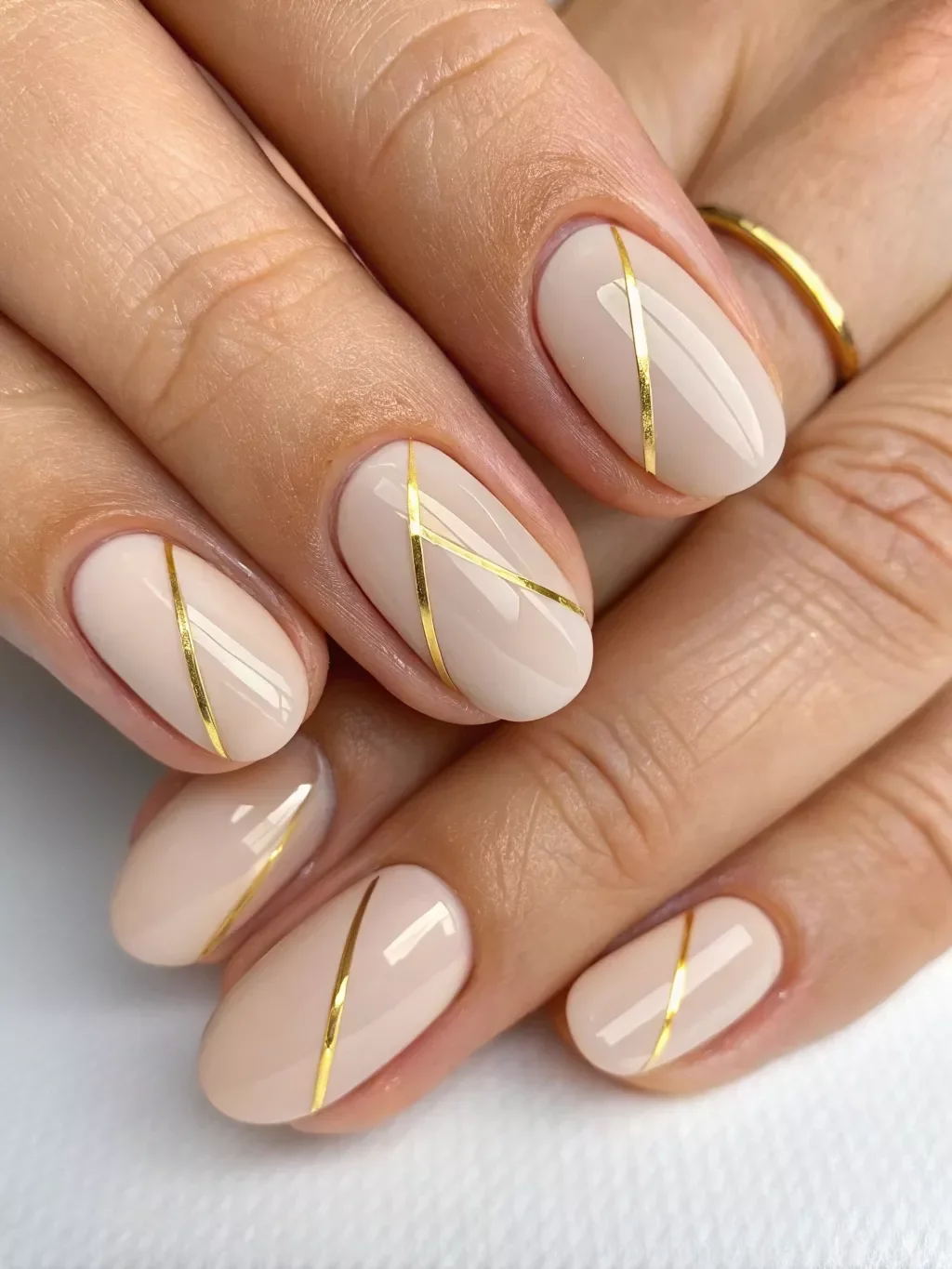 молочно-бежевое покрытие на овальных ногтях с золотыми диагональными линиями