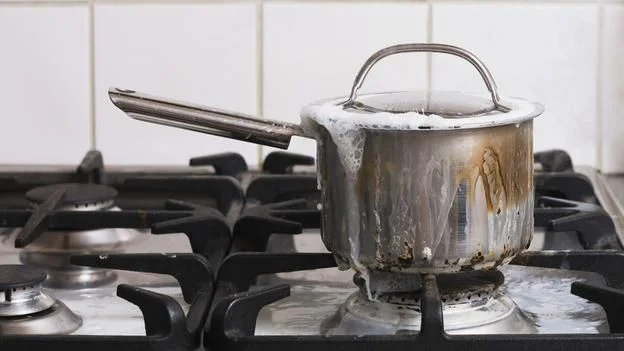 Каструля з нержавійки з потьоками збіглого й пригорілого молока на газовій плиті